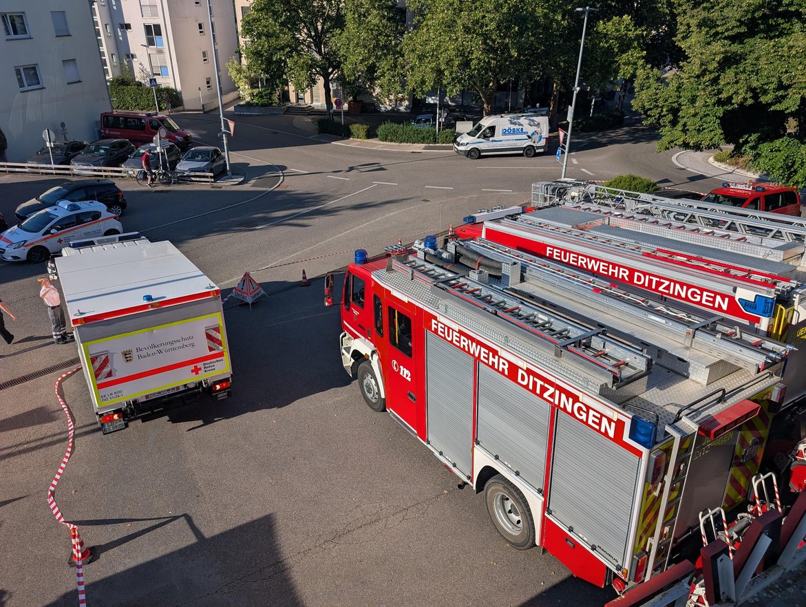 Ein Bild aus der Feuerwehrwache Ditzingen mit Blick nach unten auf die Einfahrt. Dort stehen rechts zwei Einsatzfahrzeuge der Feuerwehr, links parkt gerade ein Fahrzeug des Deutschen Roten Kreuz rückwärts ein.