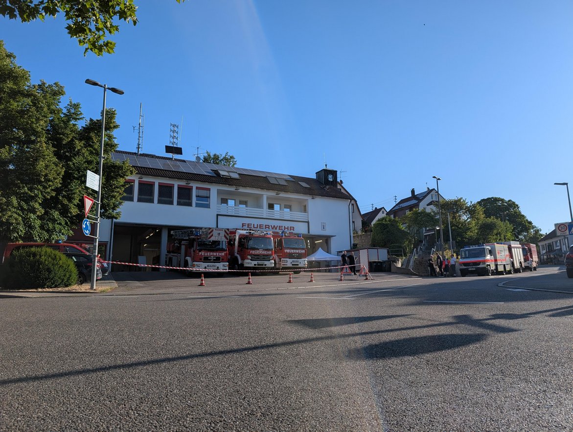 Ein Bild von der Feuerwehrwache. Man sieht drei Einsatzfahrzeuge der Feuerwehr direkt in der Einfahrt der Wache. rechts daneben sind weitere Einsatzfahrzeuge von Feuerwehr und Deutschen Roten Kreuz.